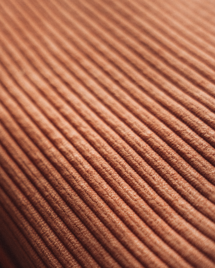 Macro close-up of a brown ribbed cloth, the corduroy wale running as even ridges across the frame.