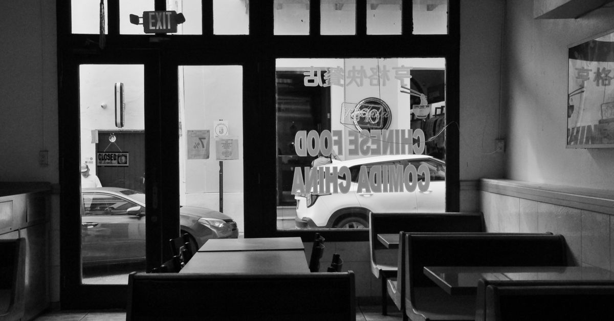 Monochrome image of a deserted Chinese restaurant interior with a street view.