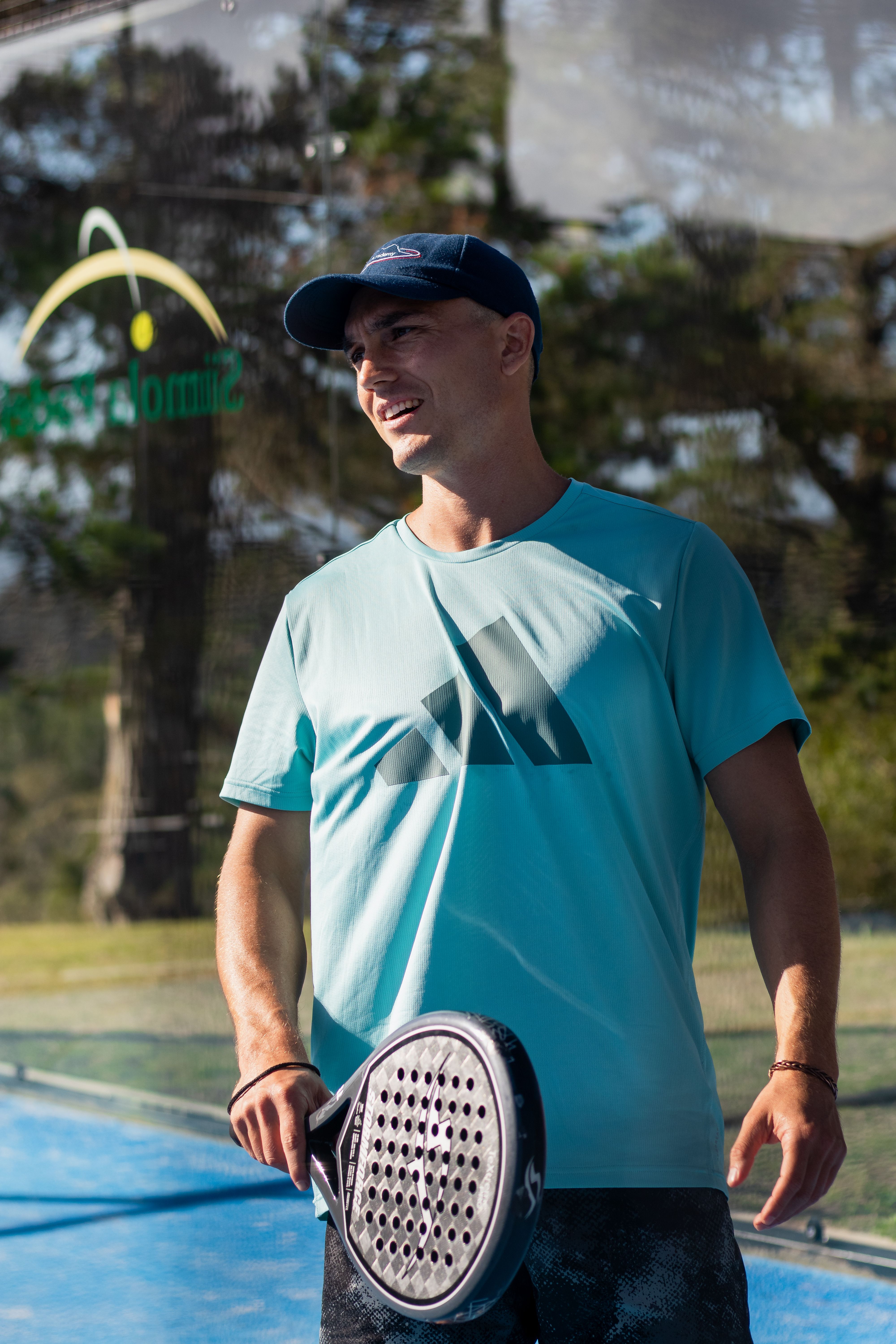 Smiling man on outdoor padel court holding a racket in sunlight.