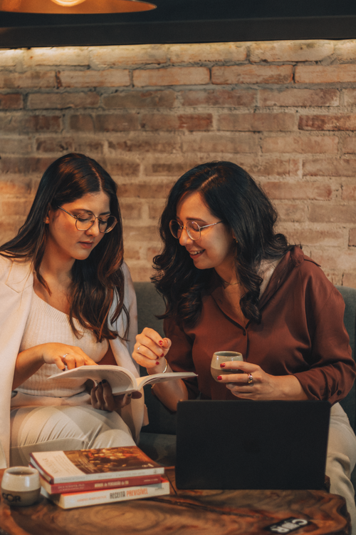 Free Two women discussing ideas with a book and laptop in a cozy cafe. Stock Photo