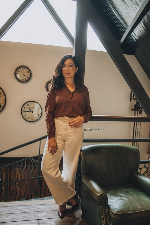 Free Confident woman in elegant attire standing in a chic loft with wall clocks. Stock Photo
