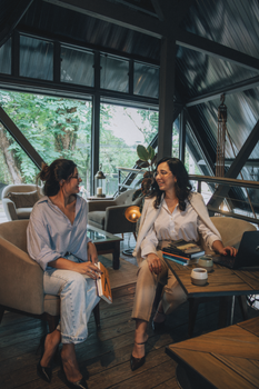 Two women engage in a friendly discussion in a stylish loft with natural light.