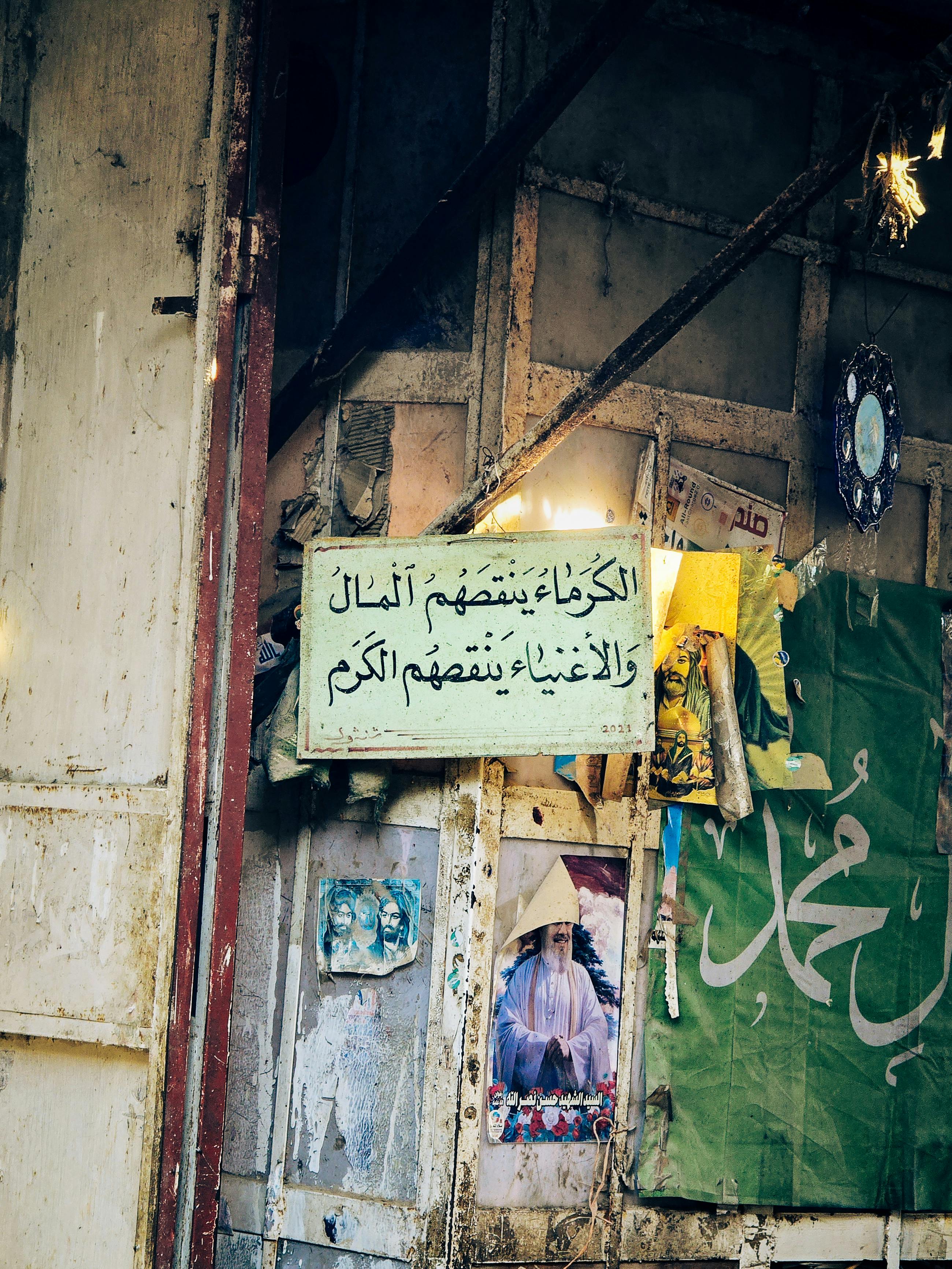 Colorful street scene featuring Arabic text and posters on a weathered wall.