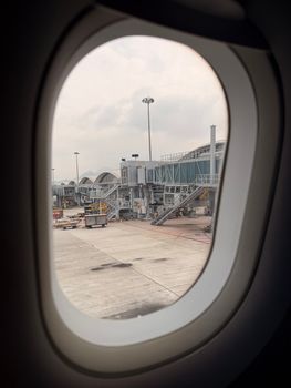 A view of Hong Kong International Airport from an airplane window, showcasing terminal structures and ground vehicles.