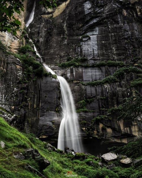 Beautiful waterfall cascade flowing through rough rocky cliff covered by green moss on sunny day