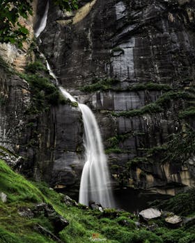 在晴天，美丽的瀑布流过覆盖着绿色苔藓的粗糙岩石悬崖