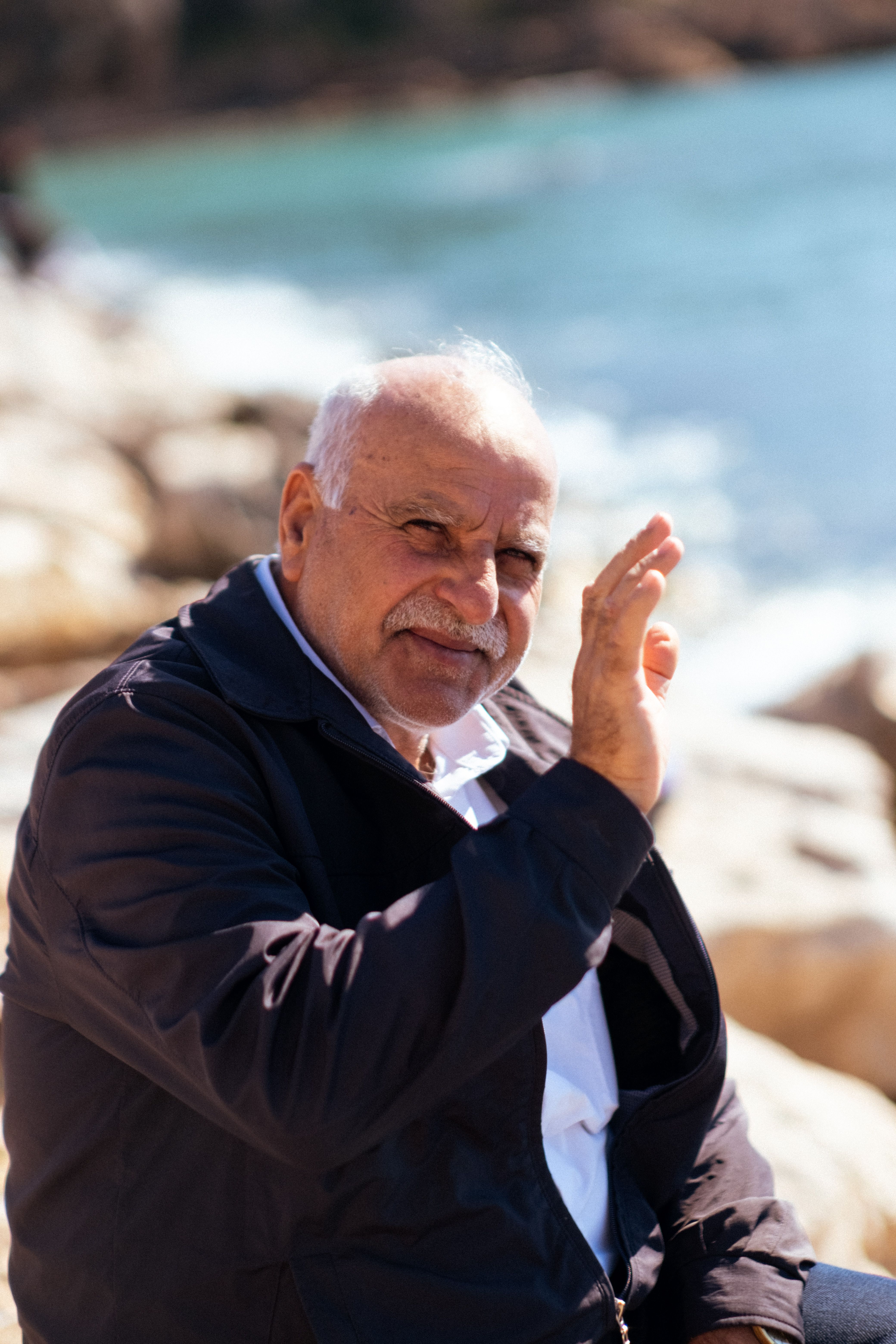 Senior man enjoying a sunny day by the sea, waving at the camera.