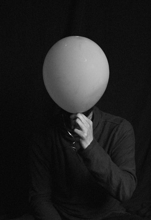 Grayscale Photo of Person Covering His Face With  Balloon