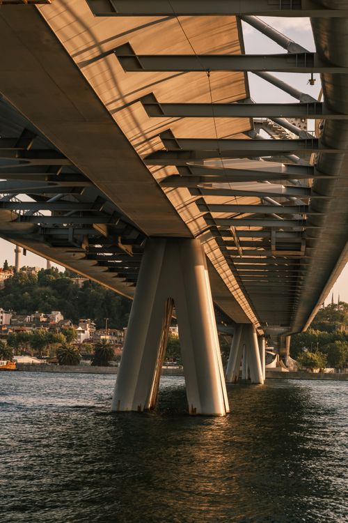 Free A detailed view of a bridge structure over calm water during sunset, showcasing architectural elements. Stock Photo