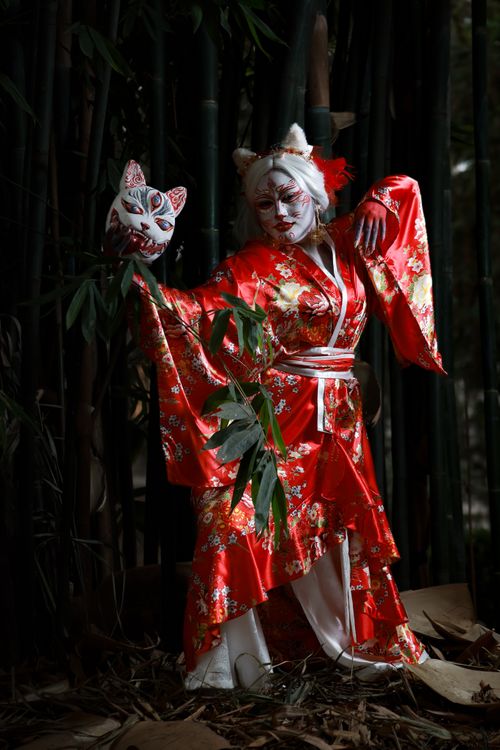 Free A person in a red kimono and mask poses in a bamboo forest, exuding fantasy artistry. Stock Photo