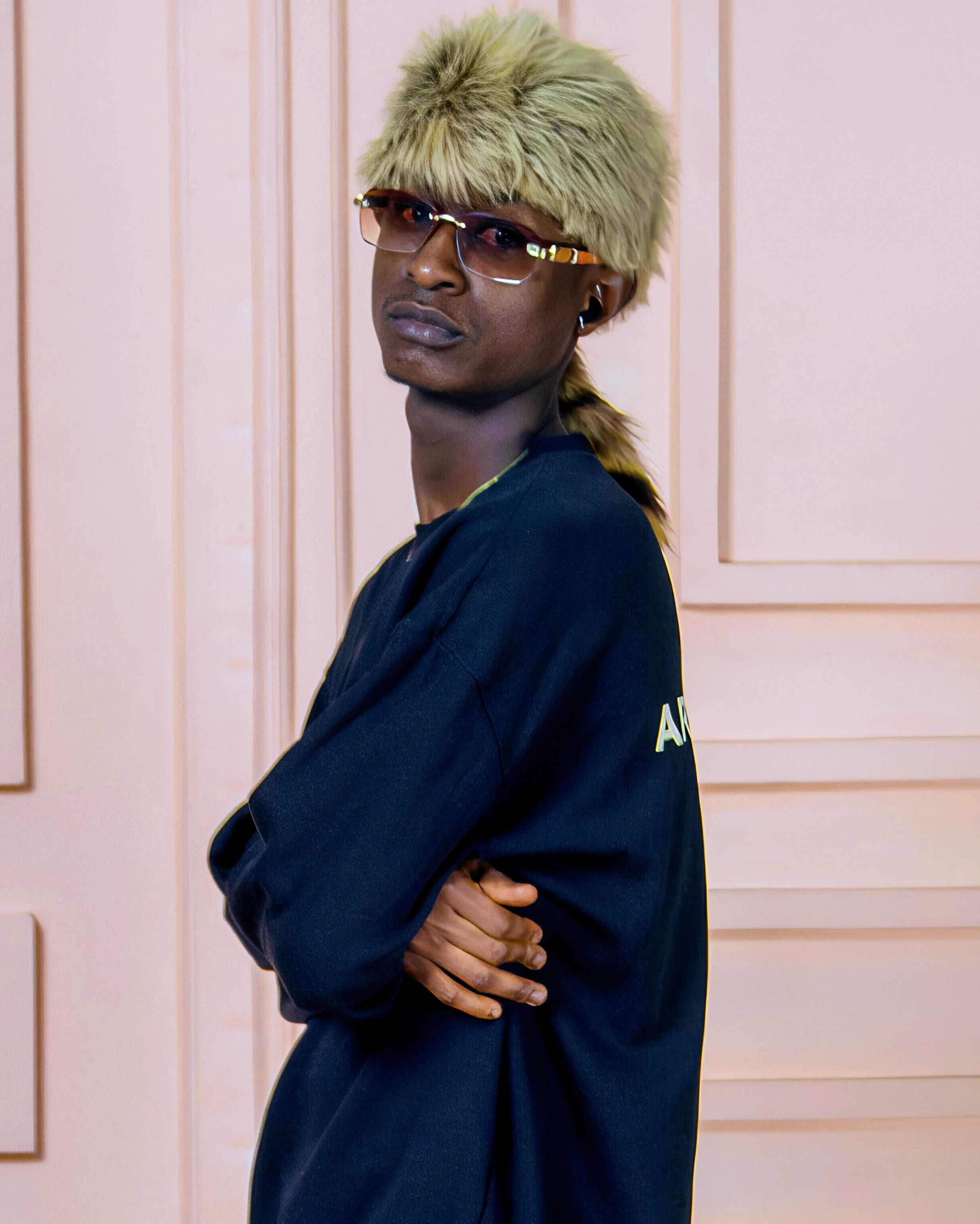 Stylish adult posing indoors wearing fashionable fur hat and sunglasses.