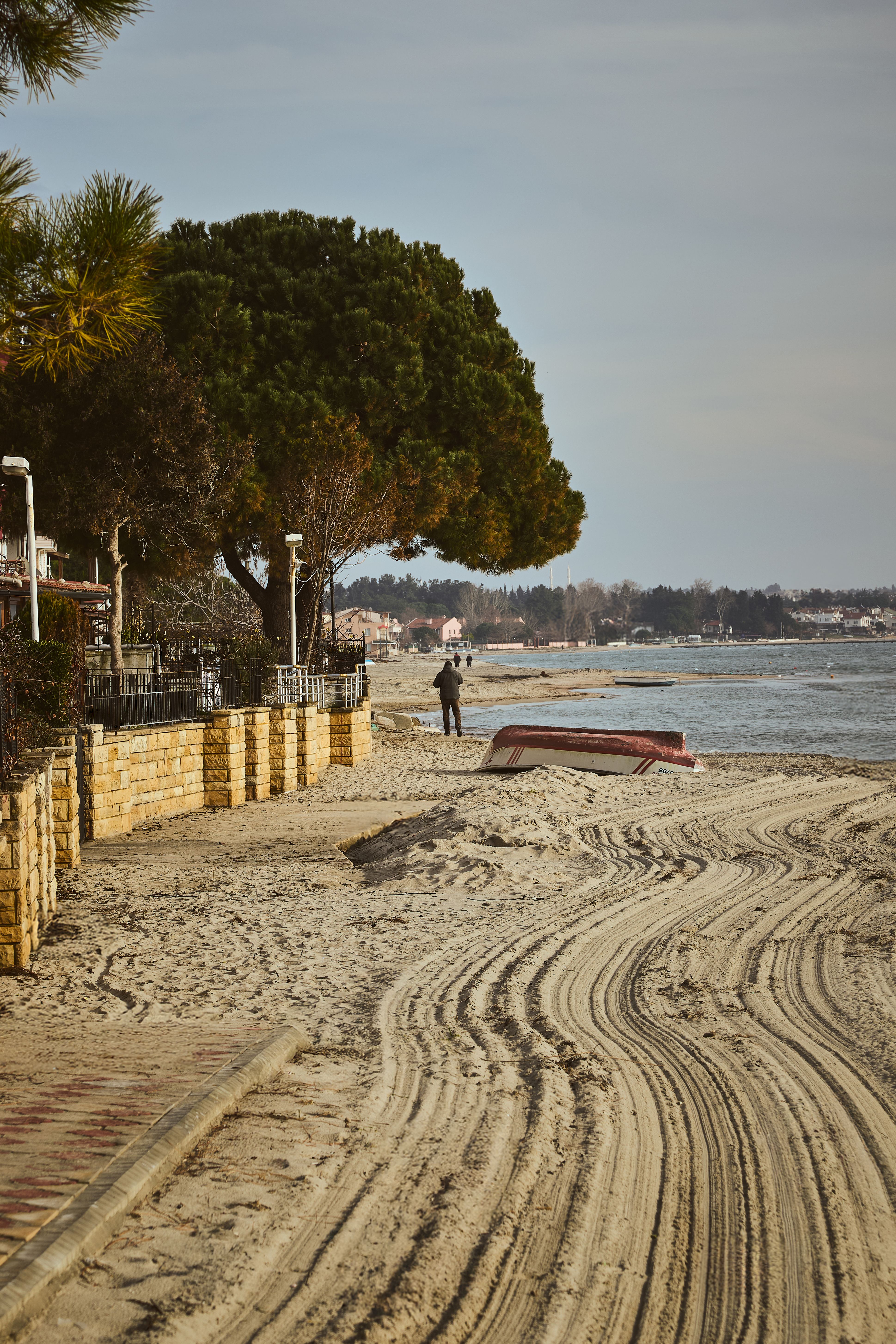 A peaceful beach scene depicting a lone walker on a sandy path lined with trees during sunset.