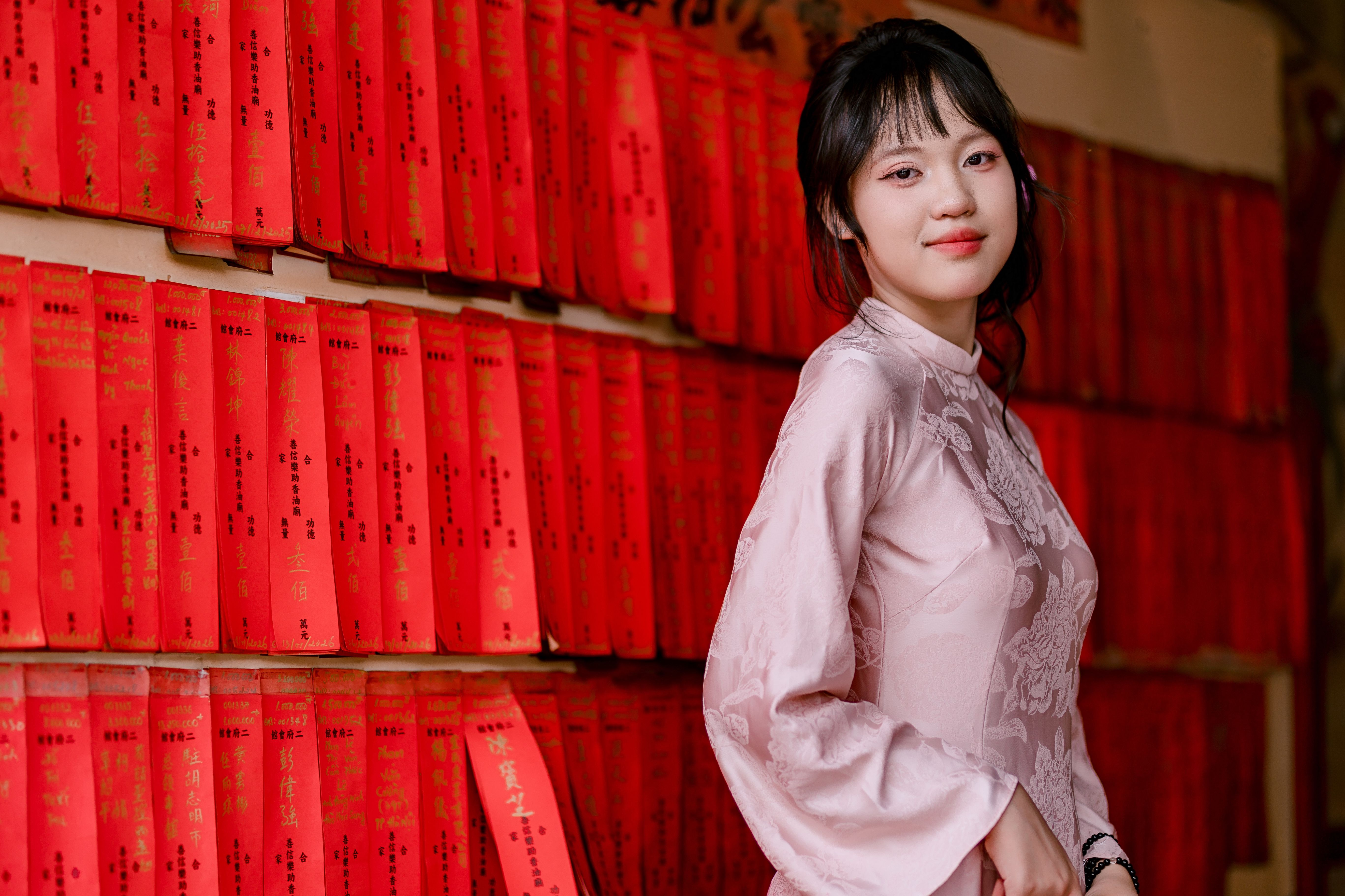 Portrait of a young woman in traditional attire posing with red scrolls as background indoors.