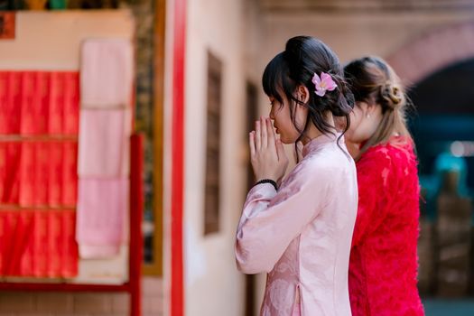 Two women in traditional dresses pray indoors, reflecting cultural values and serenity.