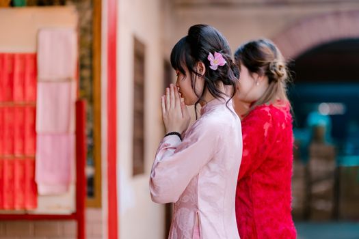 Two women praying at a temple, wearing traditional dresses, capturing a moment of reflection.