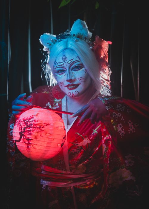 Free Geisha with intricate face paint and traditional attire holding a glowing red lantern, exuding a mystical and artistic atmosphere. Stock Photo
