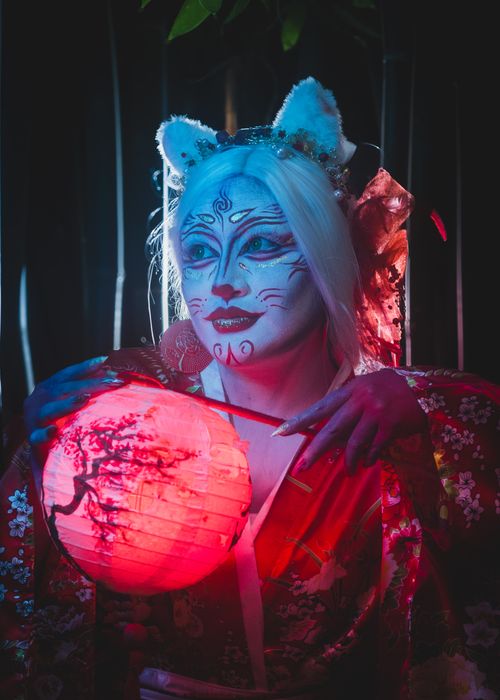 Free A captivating girl in kitsune cosplay holds a glowing lantern under vibrant lighting, evoking a mythical atmosphere. Stock Photo