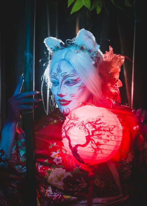 Free A captivating geisha in costume holding a glowing lantern amidst mystical darkness. Stock Photo