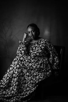 Elegant black and white portrait of a woman in floral attire sitting thoughtfully.