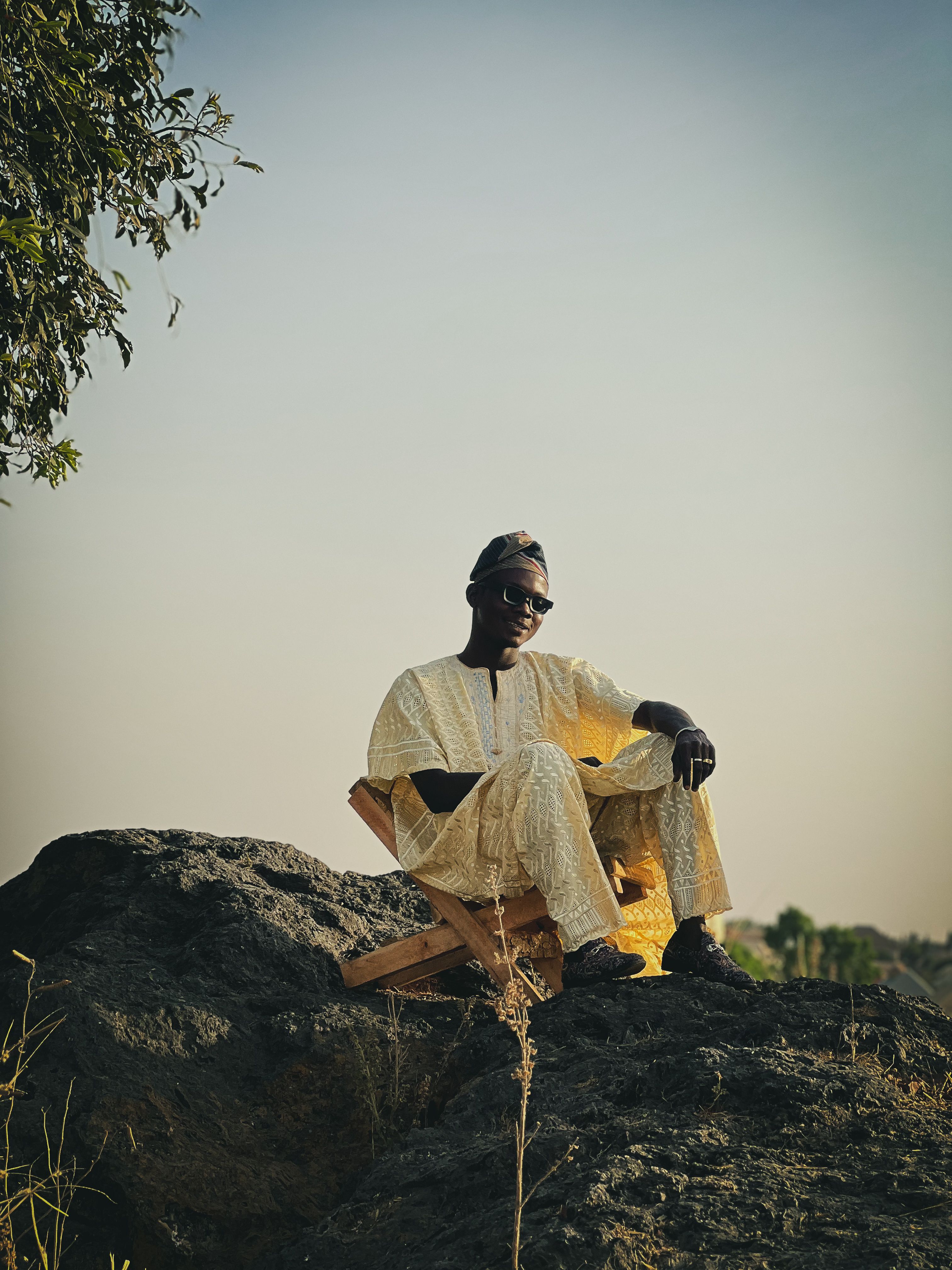 Man sitting on a rock outdoors in traditional attire under a clear sky, conveying serenity and cultural richness.