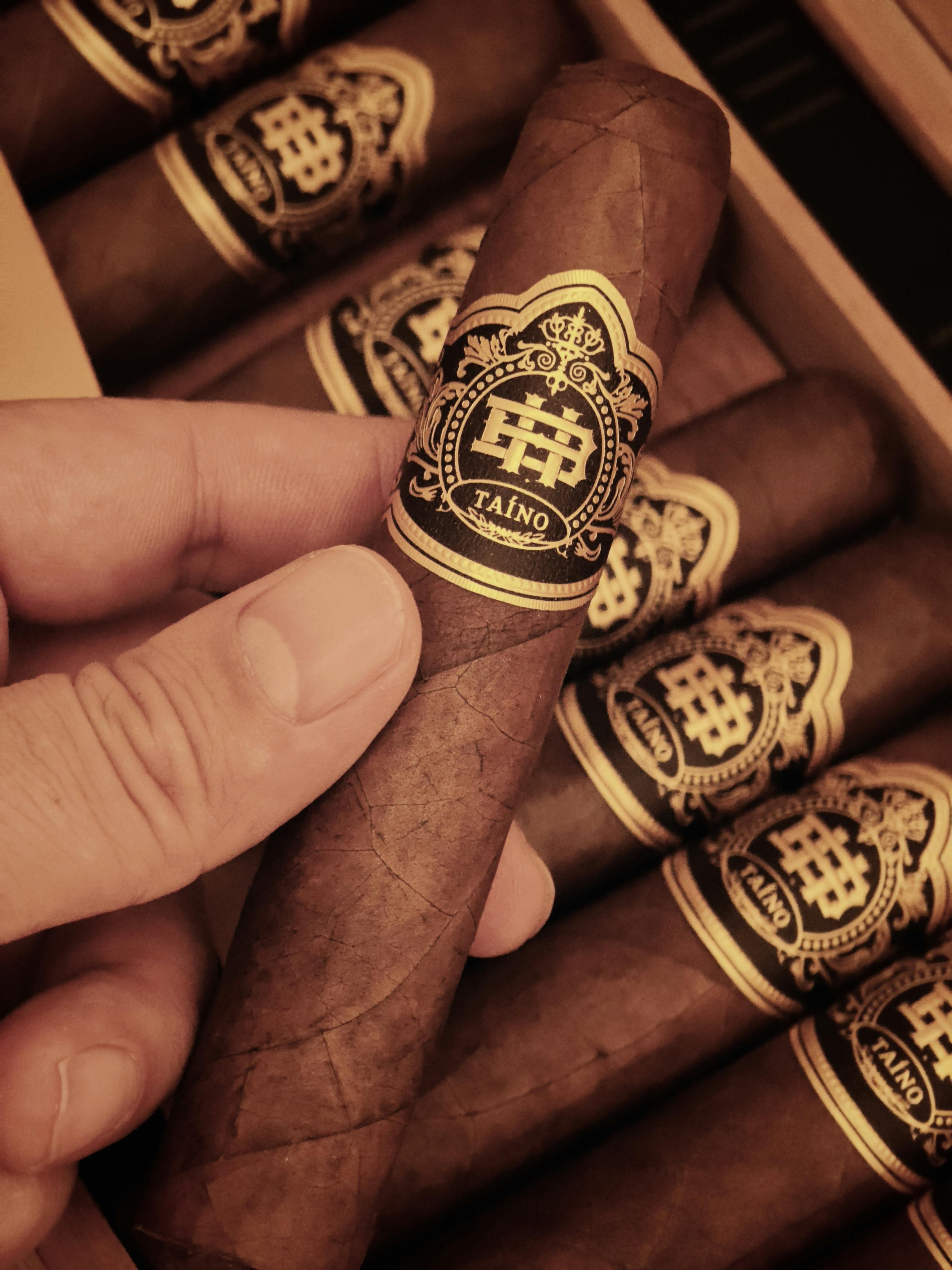 Close-up of luxury cigars held in hand, showcasing intricate packaging design in a warm tone.
