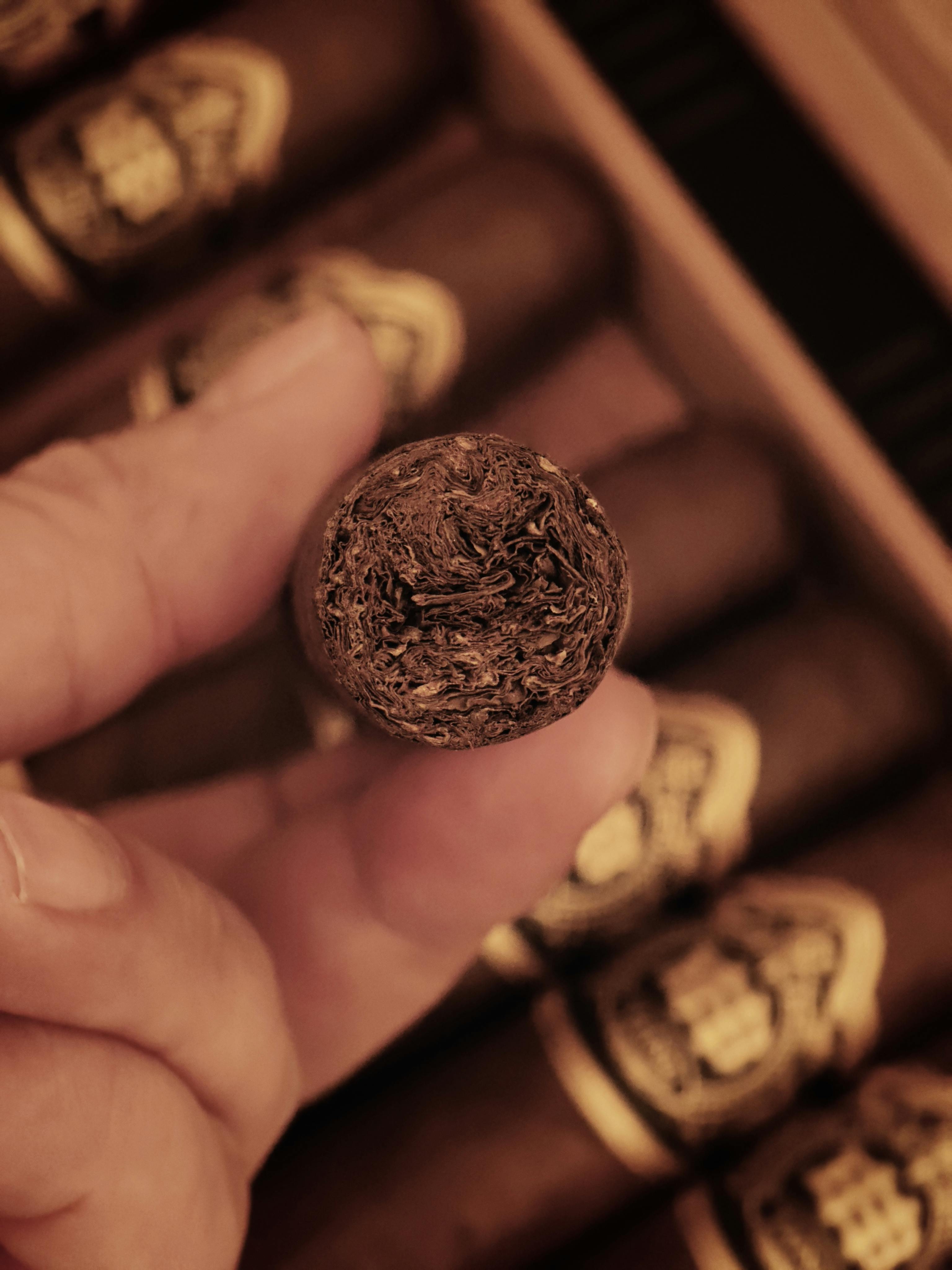 Detailed close-up of a hand holding a cigar with more cigars in the background.