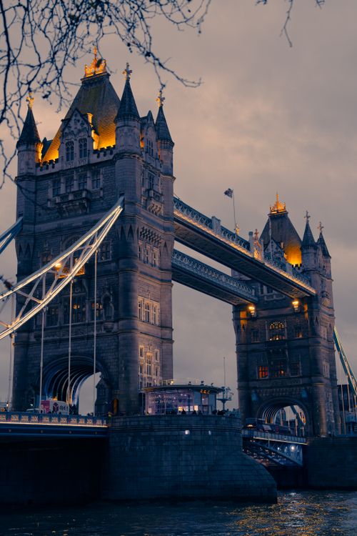 Free Tower Bridge in London beautifully lit during twilight, showcasing its Gothic architecture against a moody sky. Stock Photo