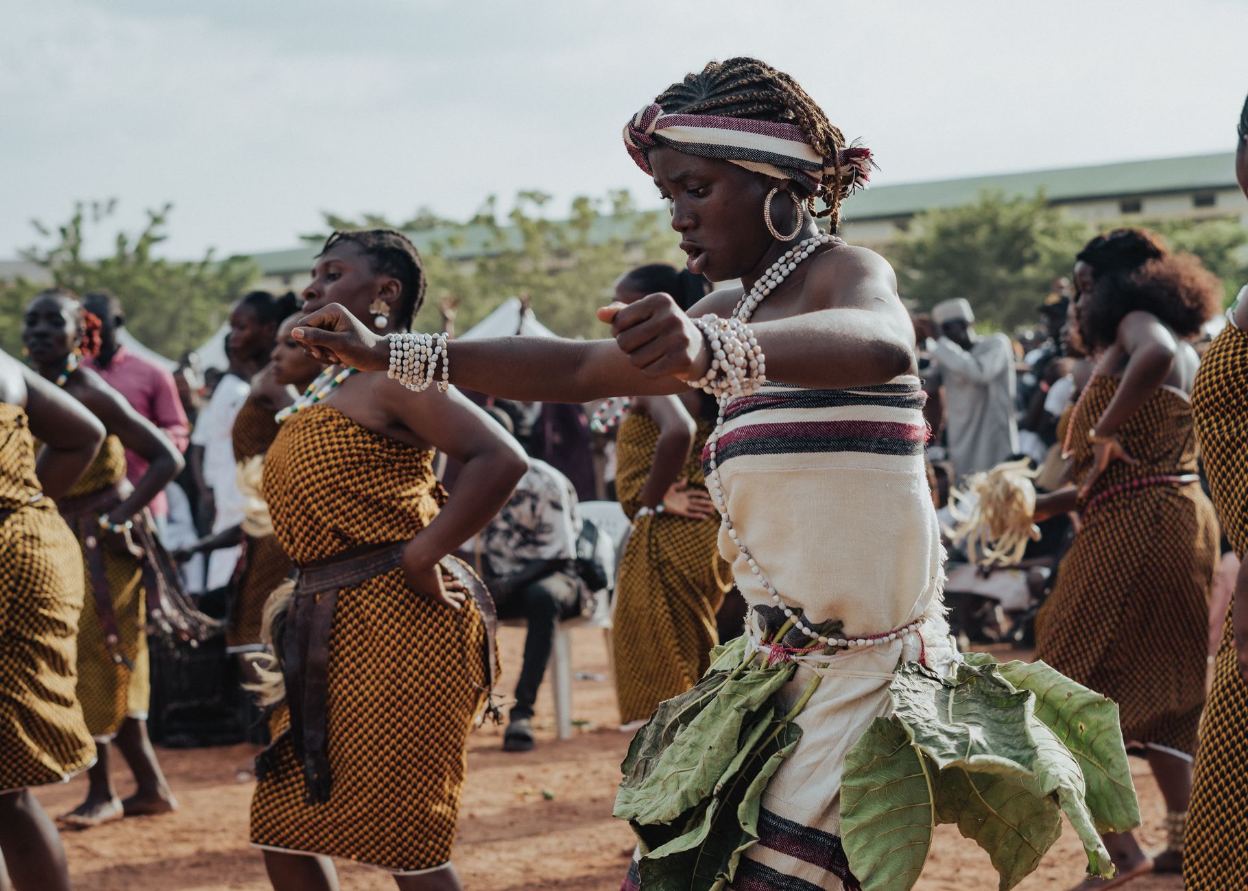 African women performing a vibrant traditional dance outdoors, showcasing cultural attire and expressions.