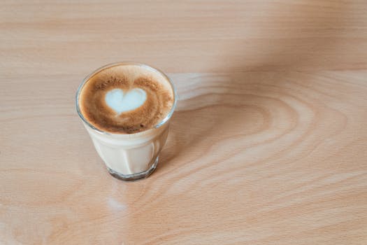 A cup of cappuccino with heart-shaped latte art on a wooden table surface.