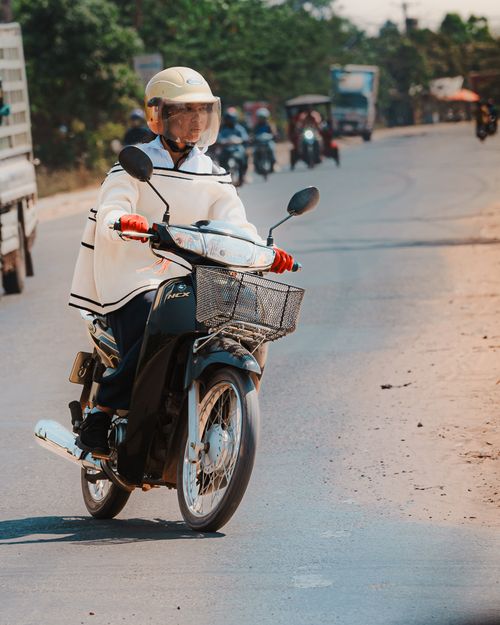 Free A helmeted scooter rider travels on a sunny Cambodian road, showcasing local transport culture. Stock Photo