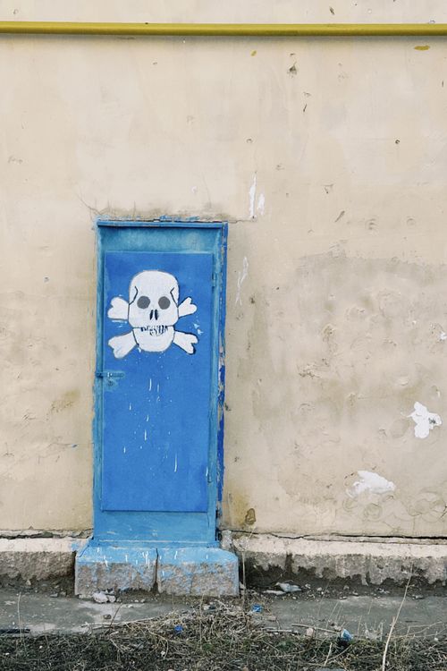 Free A blue door with a skull and crossbones painting on a weathered wall in Almaty, Kazakhstan. Stock Photo
