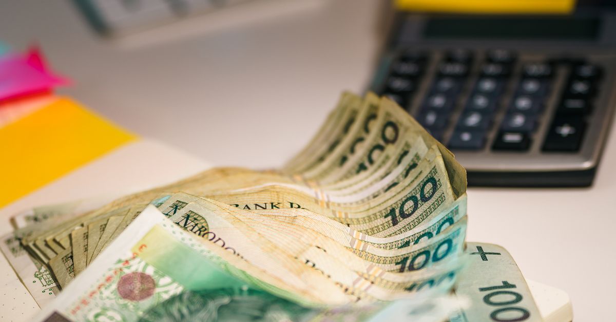Close-up of a hand using a calculator with cash and a notebook on a wooden table.
