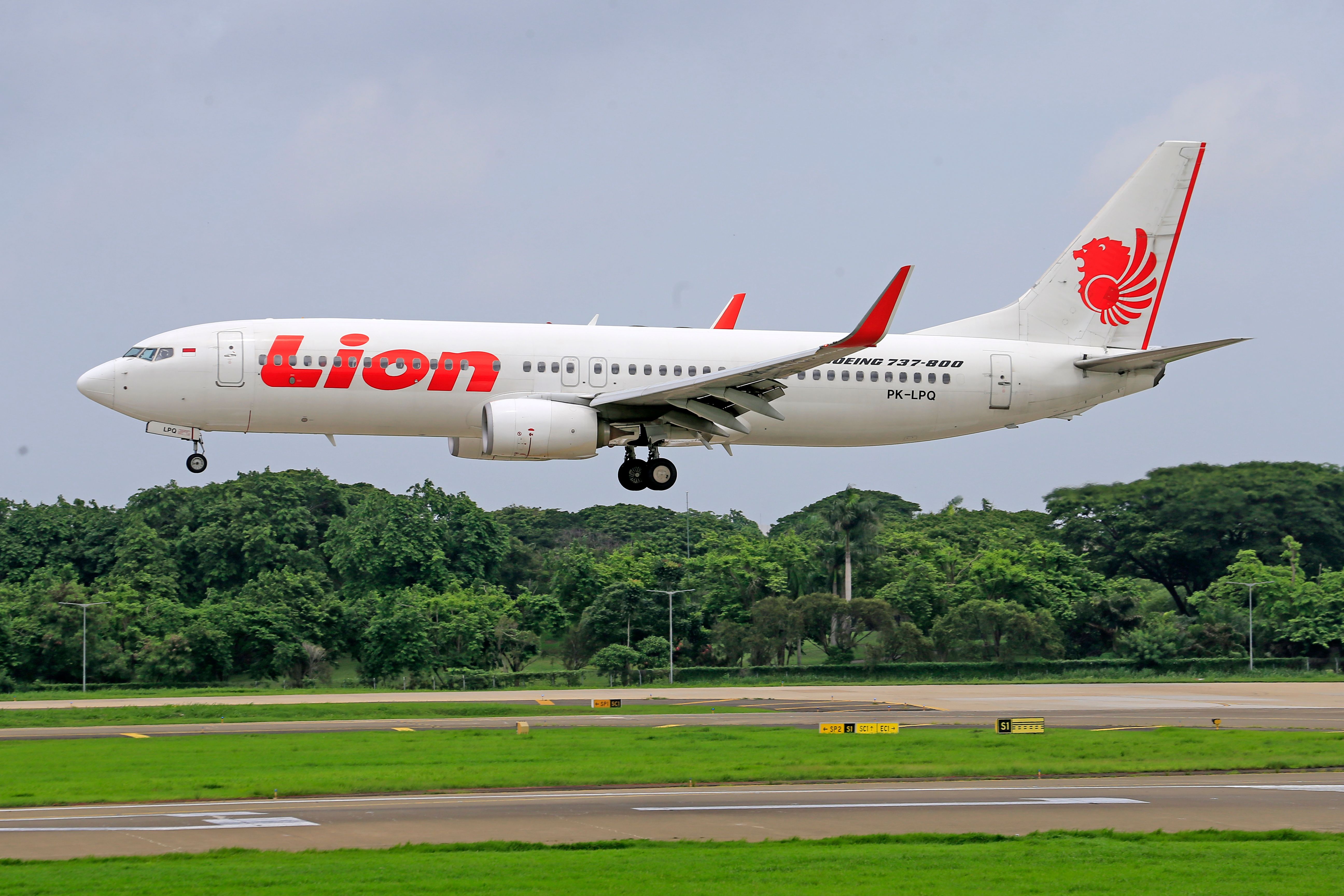 Lion Air Boeing 737 airplane landing on a runway surrounded by greenery.