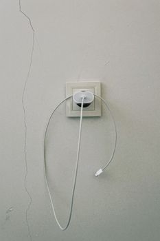 A minimalist view of a wall socket with a charging cable against a textured wall in Kazakhstan.