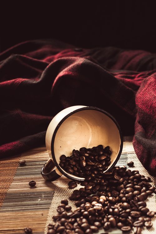 Free Spilled coffee beans from a rustic cup on a textured surface with a cozy blanket background. Stock Photo