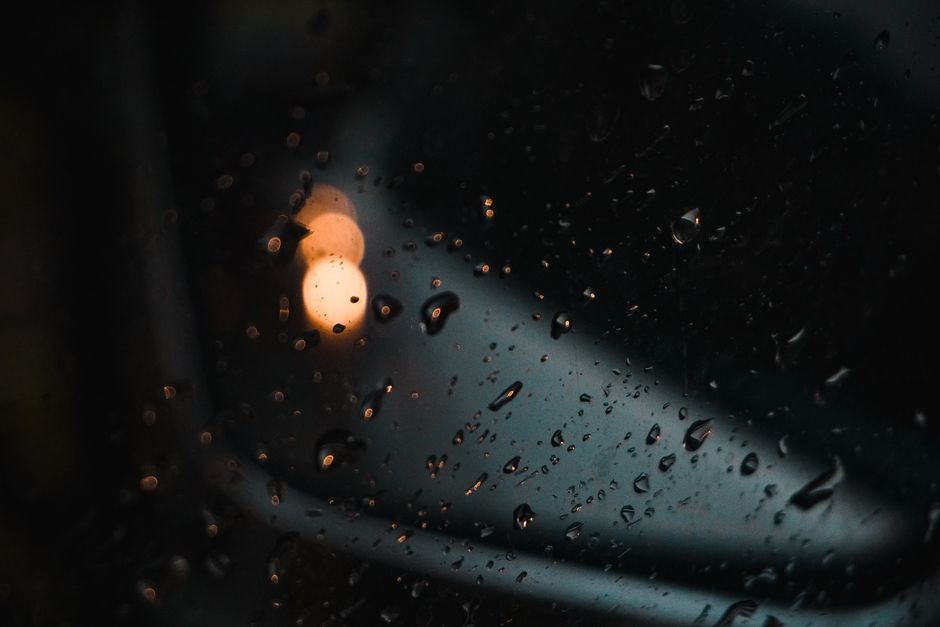 Close-up of raindrops on glass with blurred evening lights in the background.