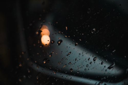 Free Close-up of raindrops on glass with blurred evening lights in the background. Stock Photo