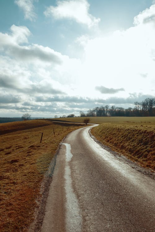 Gray Asphalt Road Between Brown Grass Field Under White Cloudy Sky