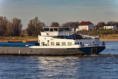 Free A cargo ship cruises through a picturesque inland waterway with charming houses in the background. Stock Photo