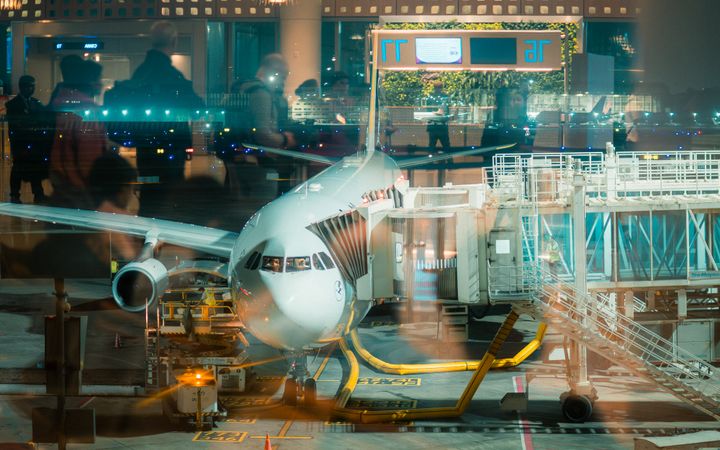 A parked airplane at Mumbai Airport gate with reflections, captured during the night.