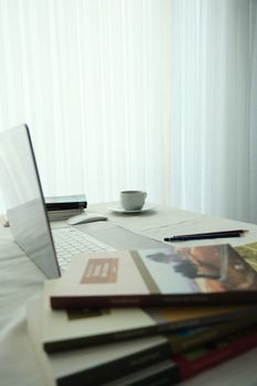 A clean, minimalist workspace featuring a laptop, books, and a coffee cup by a window.
