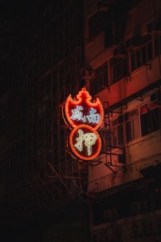Close-up of a glowing neon sign on a building facade in Hong Kong, captured at night with a moody ambiance.