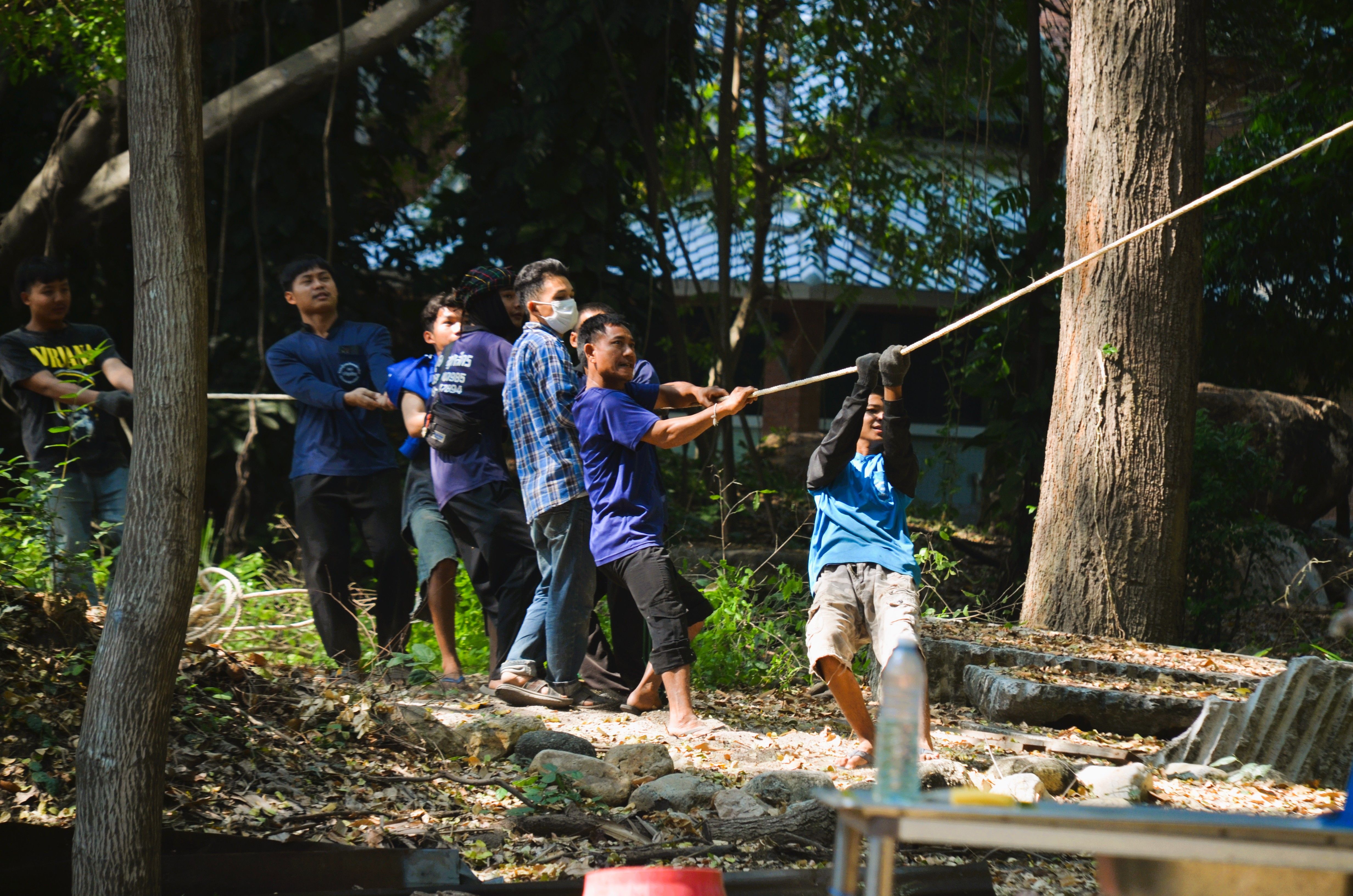 Men playing tug of war outside in a forest setting, showcasing teamwork.
