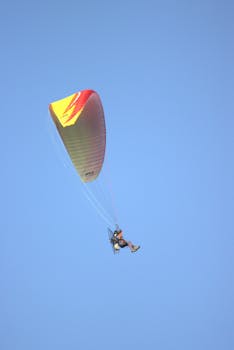 A paraglider with a colorful parachute flying against a clear blue sky backdrop.