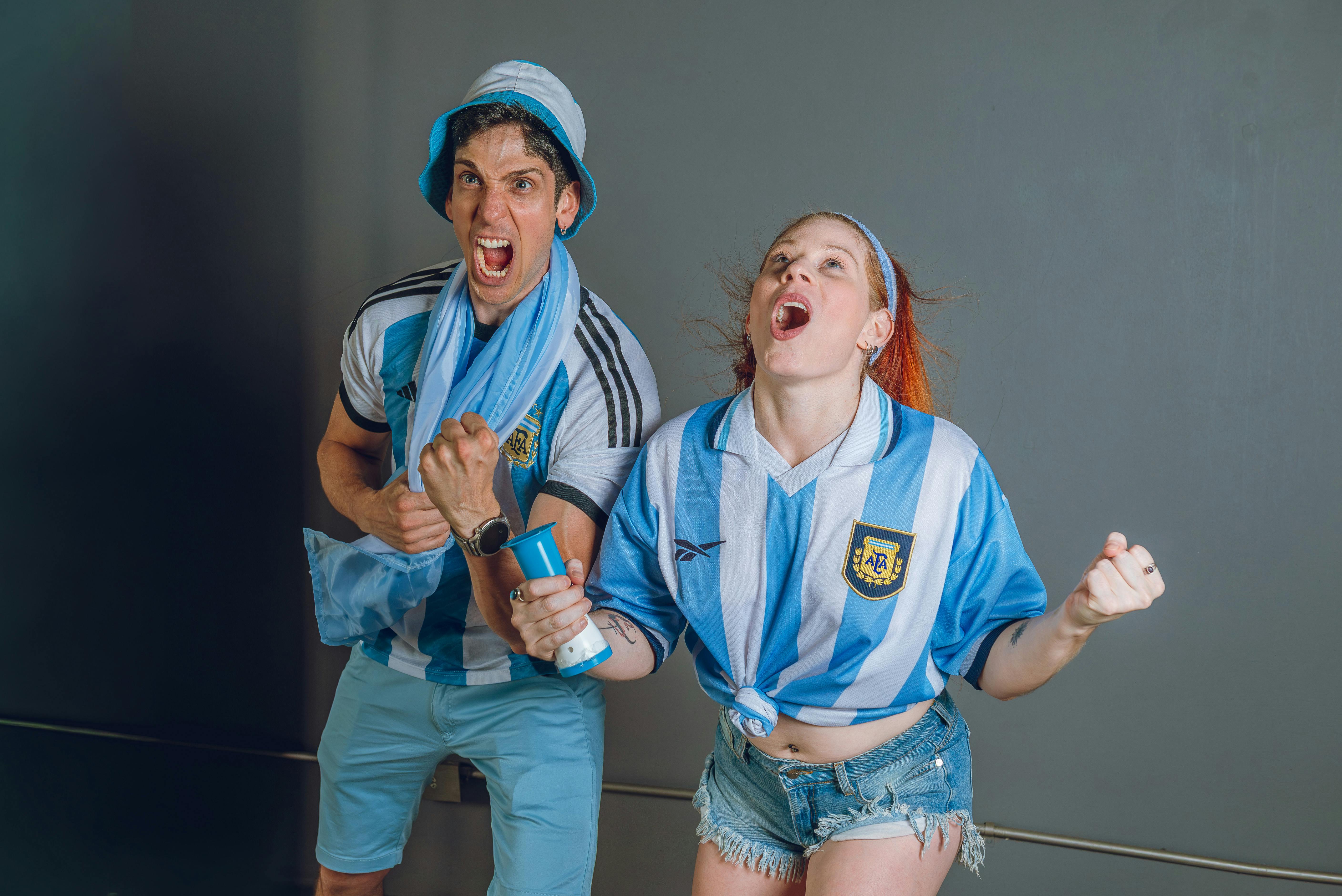 Young Argentina soccer fans in jubilant celebration with joyful expressions indoors.