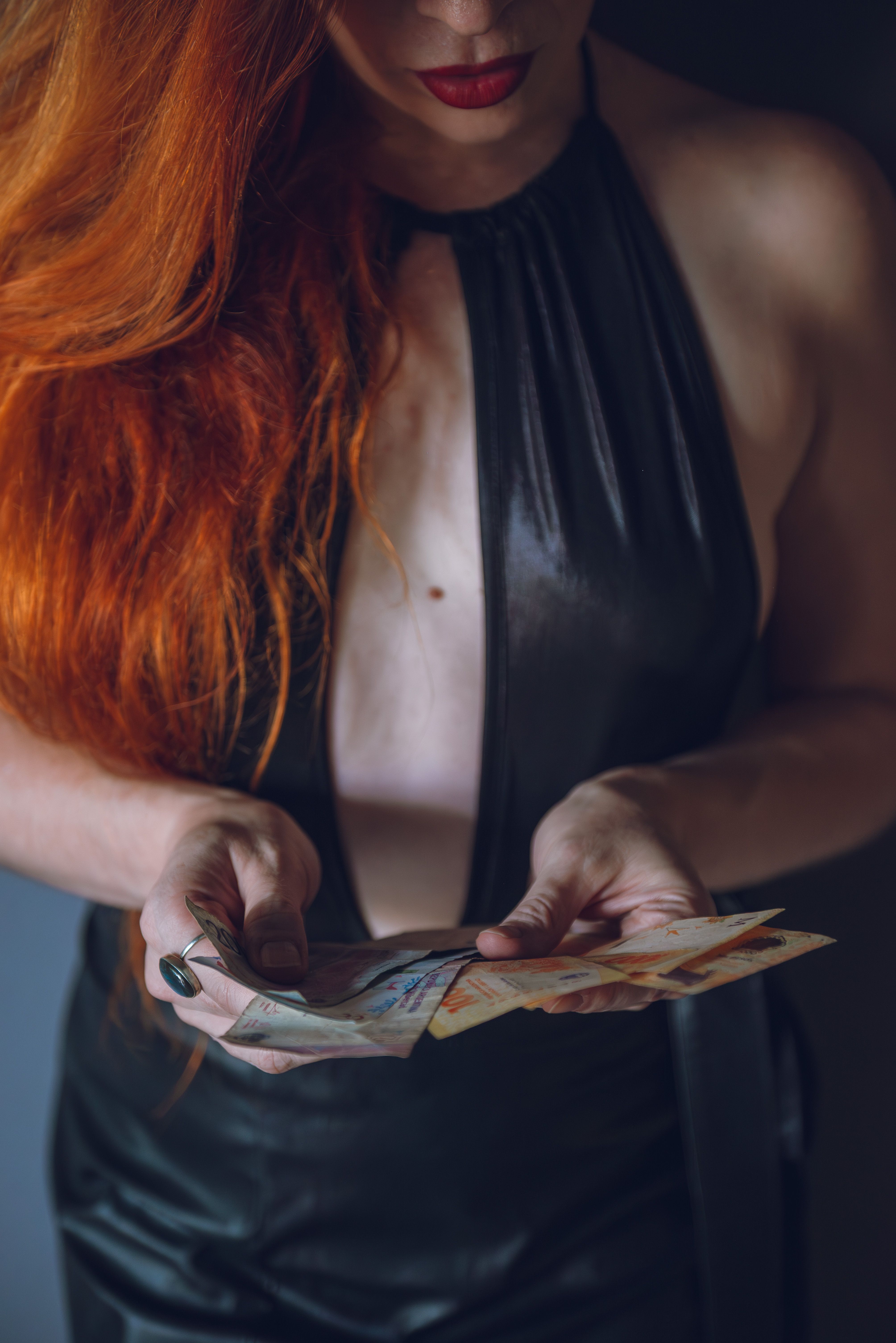 Close-up of woman with red hair in a leather outfit holding Argentine pesos.