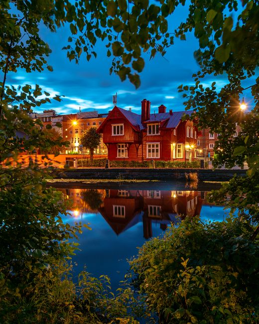 A picturesque view of a red house reflecting in the water, framed by trees in Göteborg, Sweden during twilight.