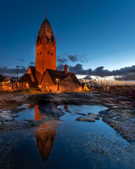 A stunning night view of a historic church in Gothenburg reflected in a puddle, showcasing architectural beauty.