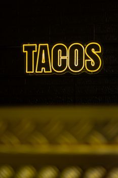 Bright neon sign displaying 'TACOS' against a dark brick wall, perfect for restaurant decor.