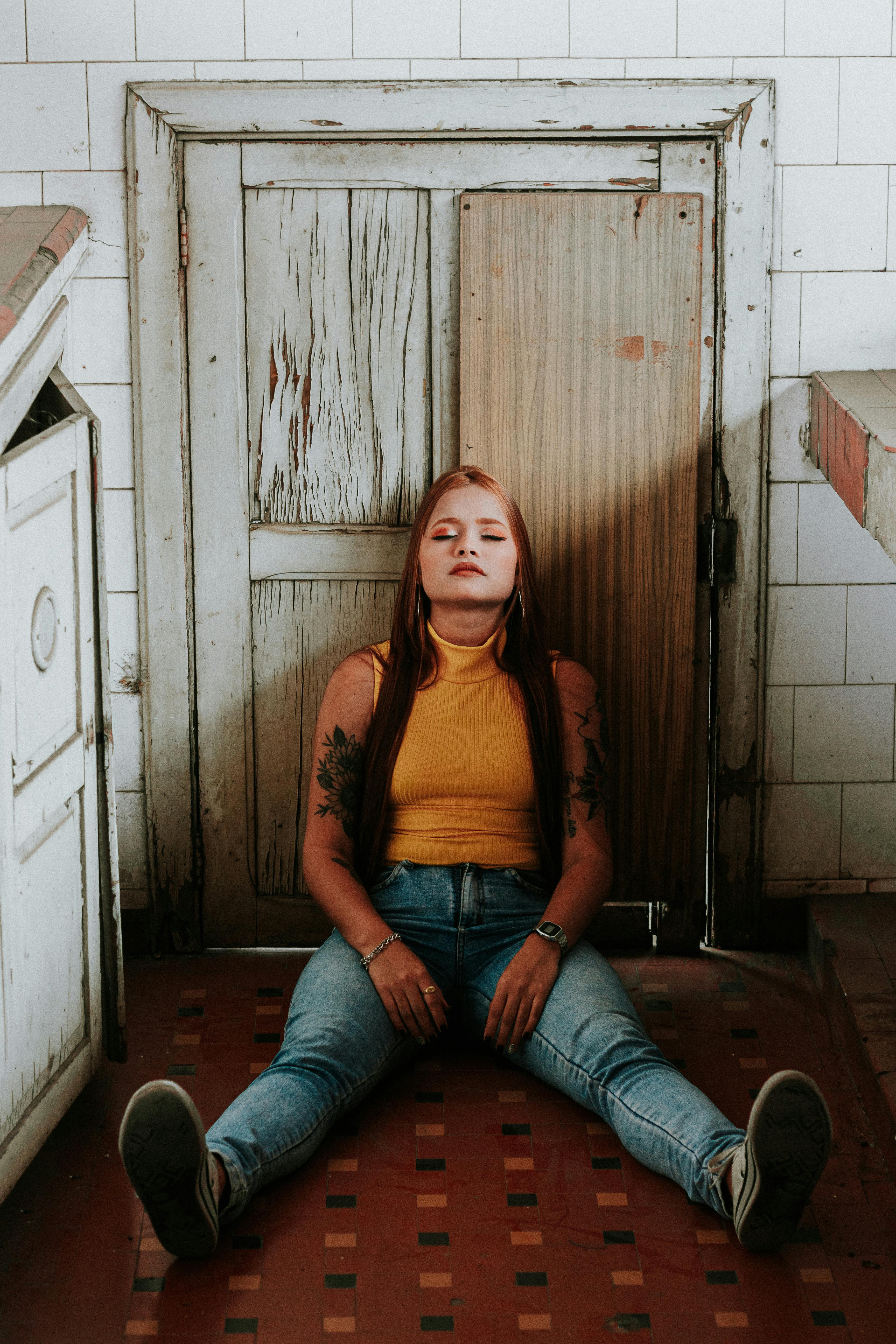 A woman in casual wear sits in a rustic indoor setting, looking relaxed and calm.